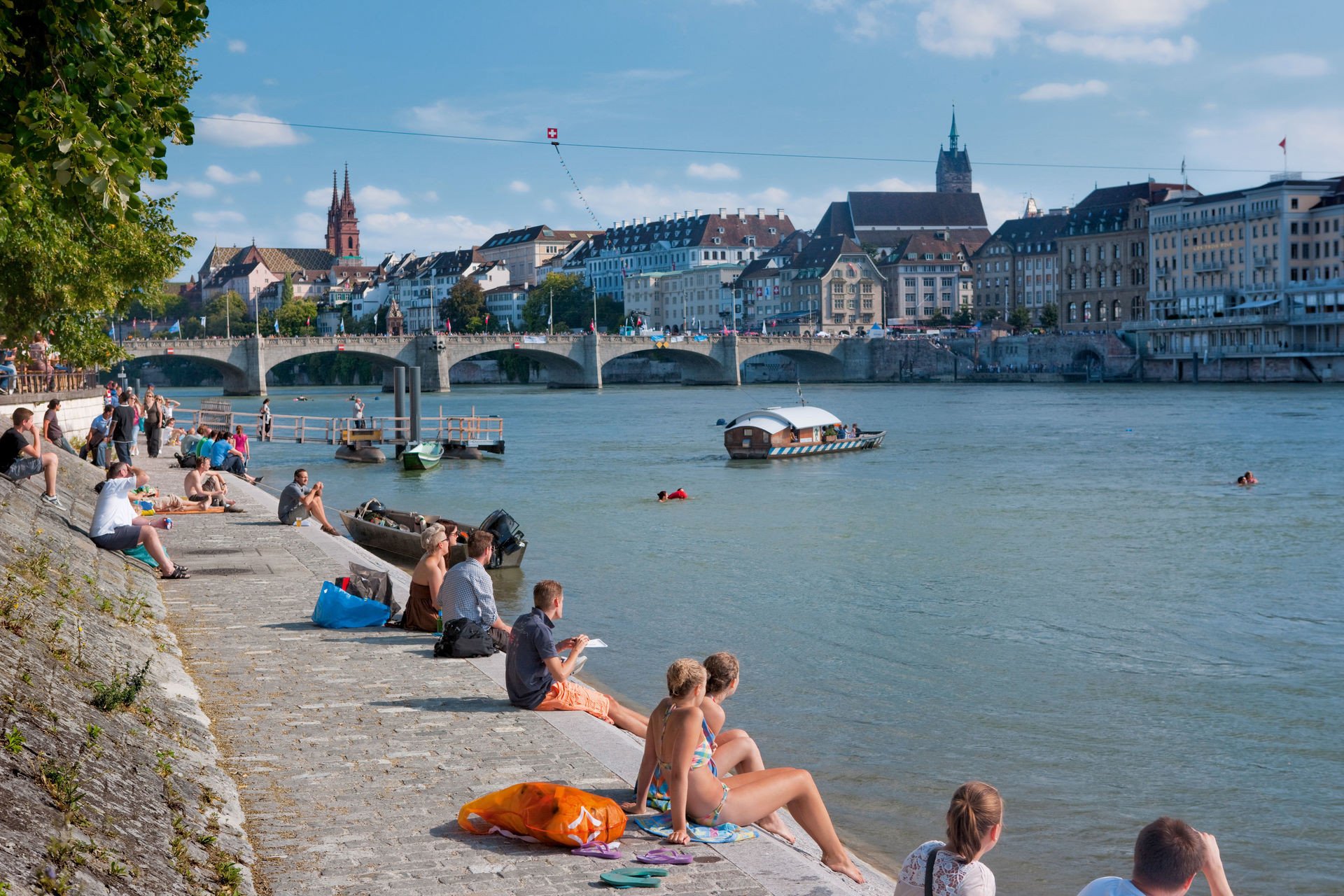 Die Kleinbasler Rheinpromenade im Sommer.
Switzerland. get natural. People enjoying the summer in the city on the banks of the Rhine in Basel, where the Klingentalfaehre (Klingental Ferry) connects the two parts of the city. In the background the Basel Cathedral, the Martins Church and on the far right: the exclusive Grand Hotel Les Trois Rois. Schweiz. ganz natuerlich. Die Bewohner von Basel geniessen den Sommer am Rheinufer zwischen Mittlerer Bruecke und Johanniterbruecke. Im Vordergrund die Klingentalfaehre, im Hintergrund das Basler Muenster, die Martinskirche und ganz rechts das Grand Hotel Les Trois Rois.Suisse. tout naturellement. Les gens aiment l'ete sur les rives du Rhin. En premier plan, le traversier de Klingental, au fond a gauche, la cathedrale de Bale, l'eglise Saint-Martin et a droite, l'exclusive Hotel Les Trois Rois.Copyright by: Switzerland Tourism By-Line: swiss-image.ch/Christof Sonderegger