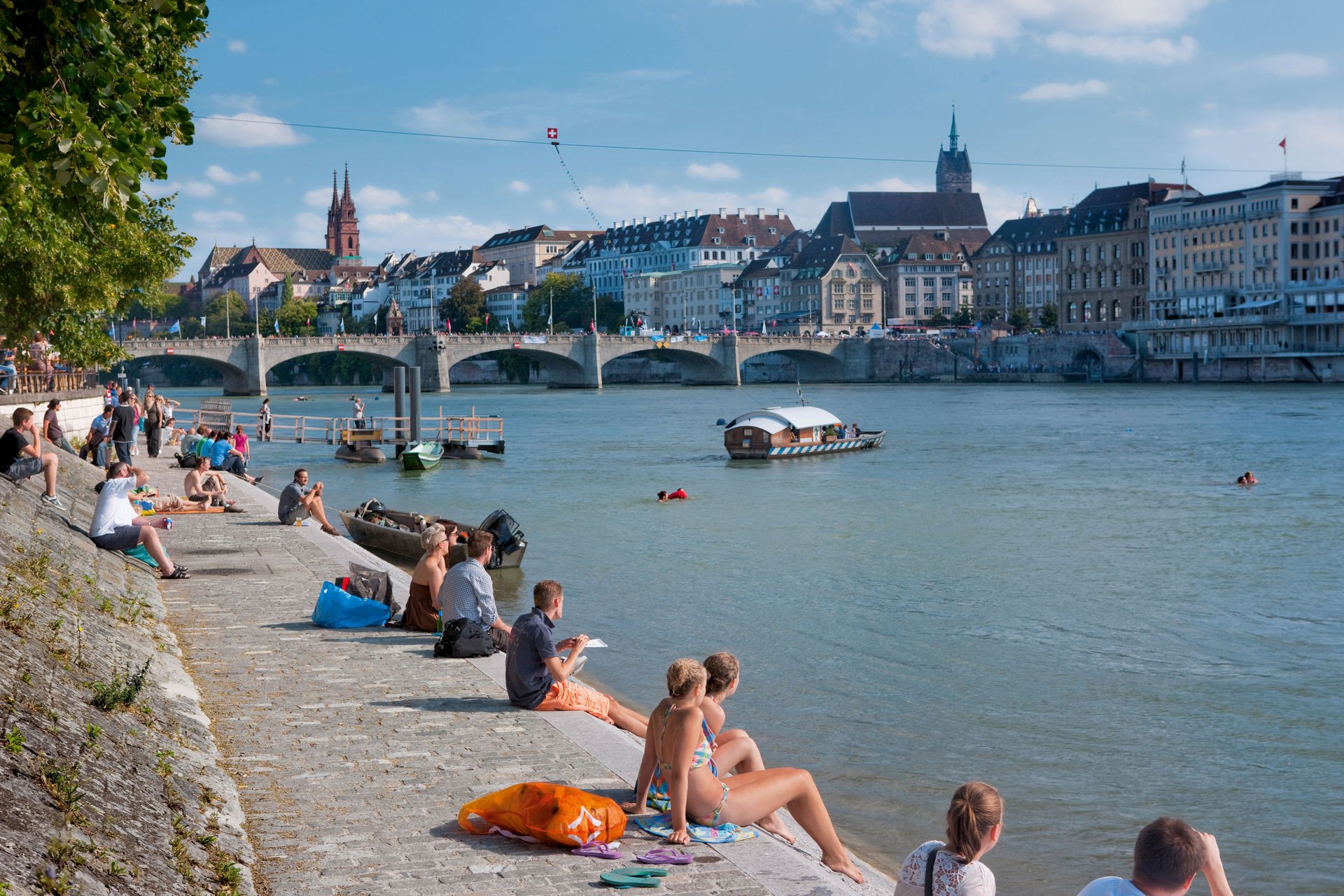 Die Kleinbasler Rheinpromenade im Sommer.
Switzerland. get natural. People enjoying the summer in the city on the banks of the Rhine in Basel, where the Klingentalfaehre (Klingental Ferry) connects the two parts of the city. In the background the Basel Cathedral, the Martins Church and on the far right: the exclusive Grand Hotel Les Trois Rois. Schweiz. ganz natuerlich. Die Bewohner von Basel geniessen den Sommer am Rheinufer zwischen Mittlerer Bruecke und Johanniterbruecke. Im Vordergrund die Klingentalfaehre, im Hintergrund das Basler Muenster, die Martinskirche und ganz rechts das Grand Hotel Les Trois Rois.Suisse. tout naturellement. Les gens aiment l'ete sur les rives du Rhin. En premier plan, le traversier de Klingental, au fond a gauche, la cathedrale de Bale, l'eglise Saint-Martin et a droite, l'exclusive Hotel Les Trois Rois.Copyright by: Switzerland Tourism   By-Line: swiss-image.ch/Christof Sonderegger