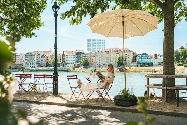 Die Künstlerin Sophie Lardon sitzt draussen in einem Kaffee am Rhein und liest in einem Magazin.