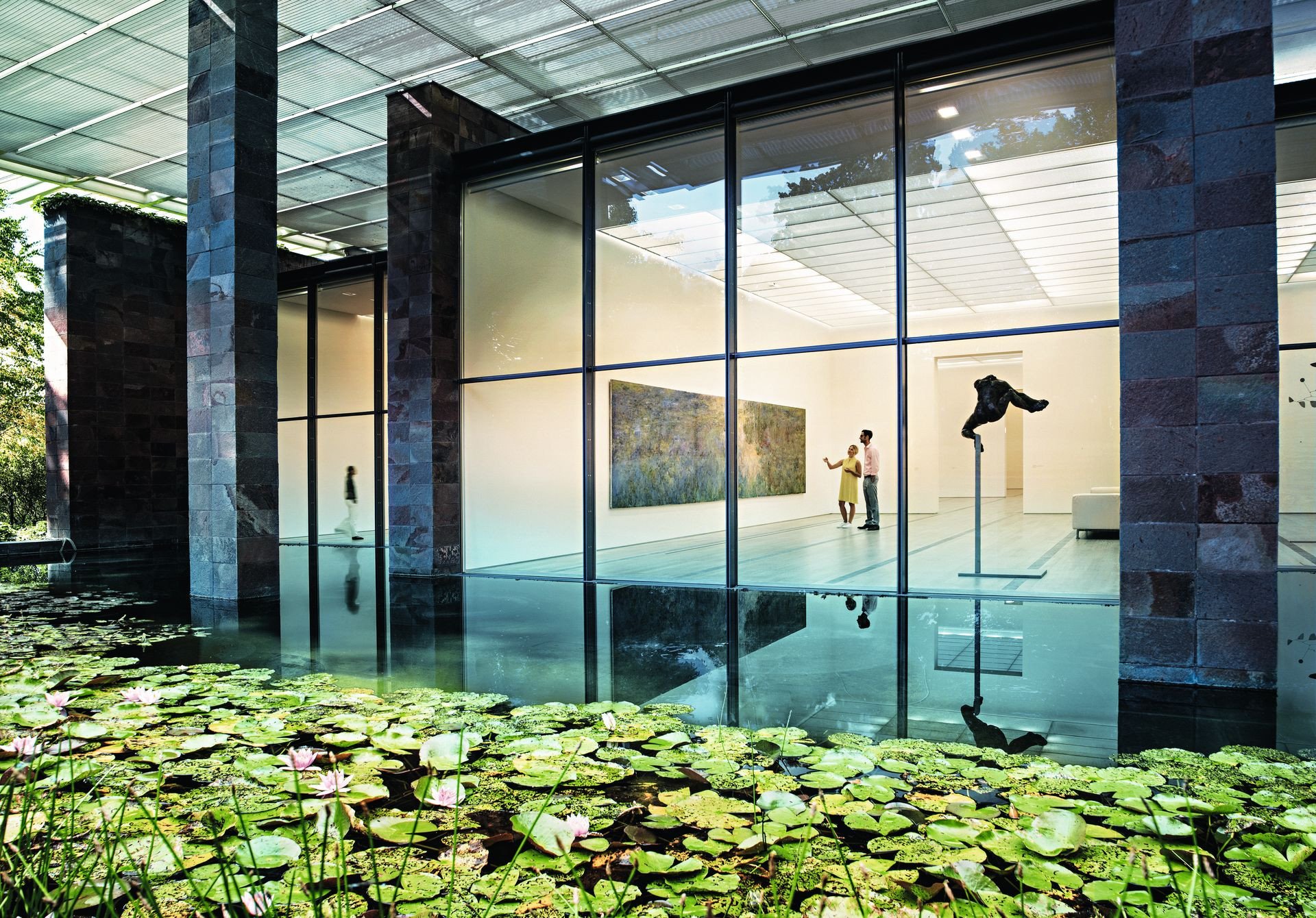 Die Fondation Beyeler in Riehen. Zentral sind Besucher zu sehen, welche das Bild Le Bassin aux nymphéas von Claude Monet betrachten, im Vordergrund der Teich mit Seerosen.