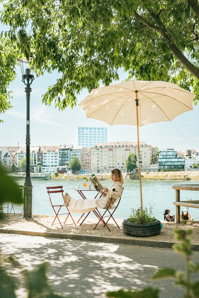 Die Künstlerin Sophie Lardon sitzt draussen in einem Kaffee am Rhein und liest in einem Magazin.